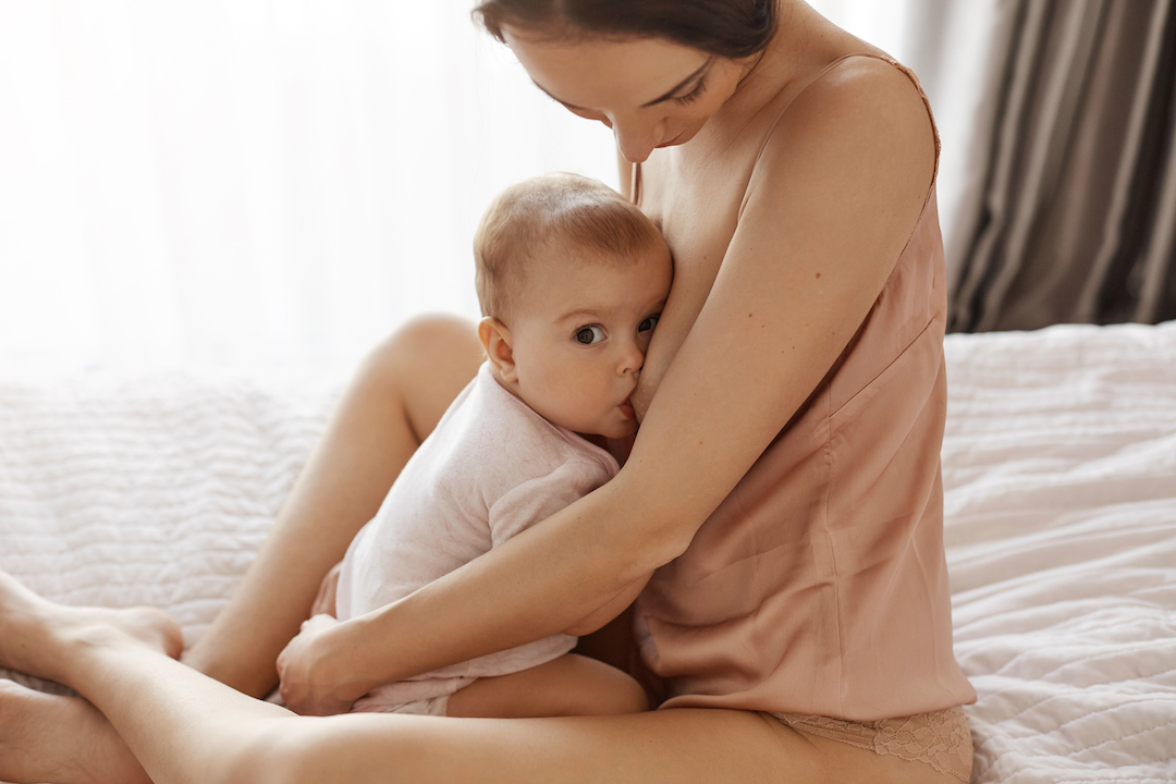 foto de una madre joven lactando a su bebé, sentados en la cama